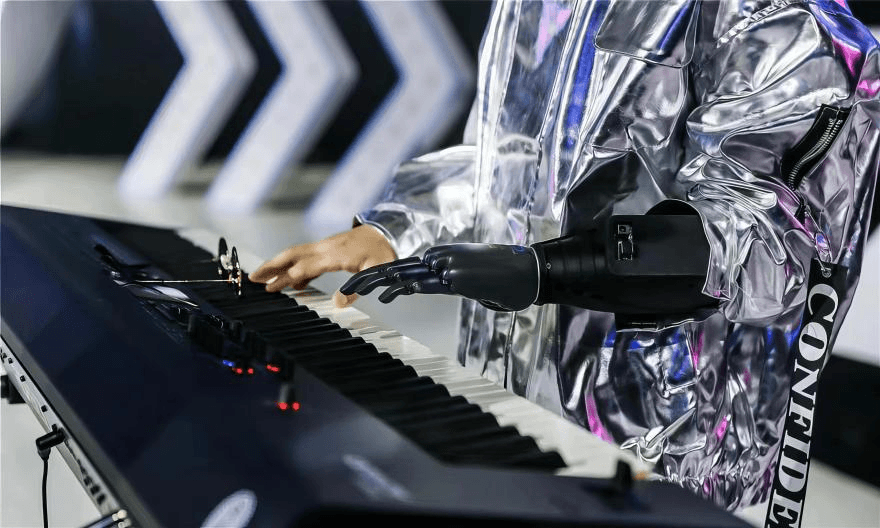 一名身着银色未来感外套的用户，正使用BrainCo智能仿生手在电子琴上弹奏，展现了技术的精准与艺术表现力。